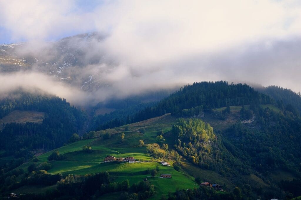 Mist-covered mountain range with lush green hills and small houses in the foreground.